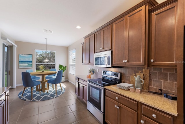 kitchen with light stone counters, stainless steel appliances, dark tile patterned flooring, visible vents, and decorative backsplash