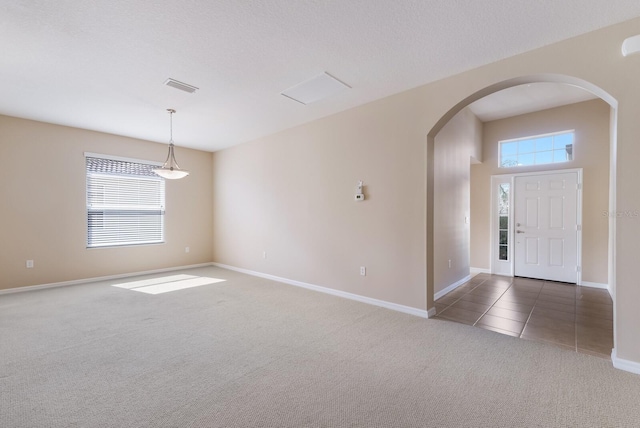 interior space featuring arched walkways, a textured ceiling, tile patterned flooring, carpet flooring, and visible vents