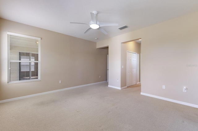 empty room with baseboards, visible vents, a ceiling fan, and light colored carpet