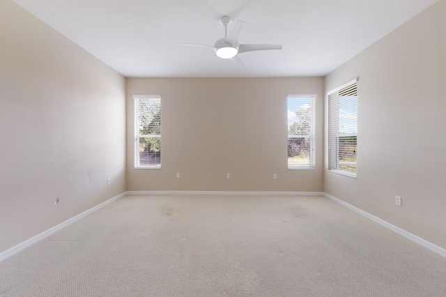 spare room with baseboards, a ceiling fan, light colored carpet, and a healthy amount of sunlight