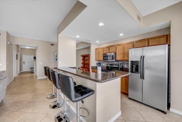 kitchen with appliances with stainless steel finishes, a center island, dark stone countertops, light tile patterned flooring, and a breakfast bar area