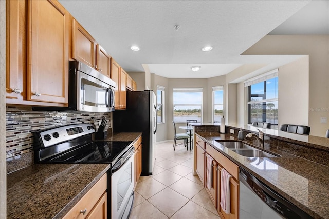 kitchen with light tile patterned floors, stainless steel appliances, decorative backsplash, dark stone counters, and sink