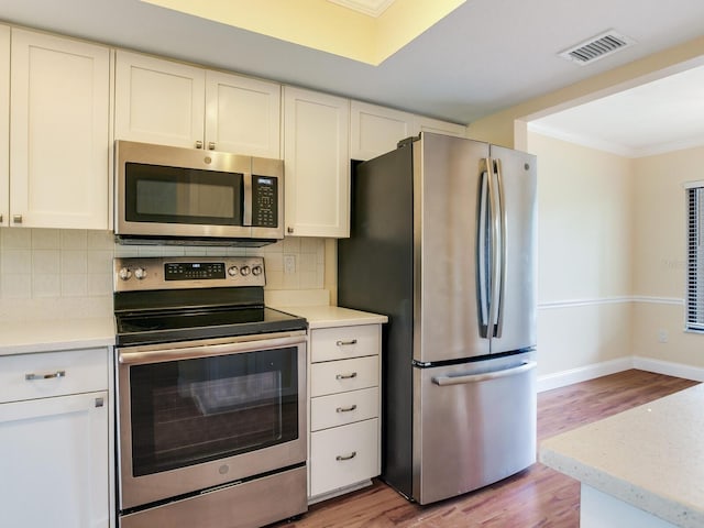 kitchen with decorative backsplash, appliances with stainless steel finishes, crown molding, light hardwood / wood-style flooring, and white cabinetry