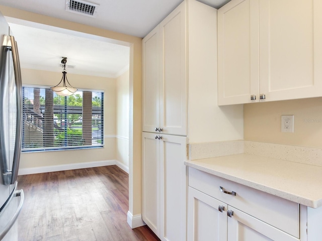 kitchen featuring stainless steel refrigerator, white cabinetry, light stone counters, and decorative light fixtures