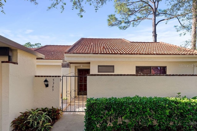 exterior space featuring a tile roof, a gate, fence, and stucco siding