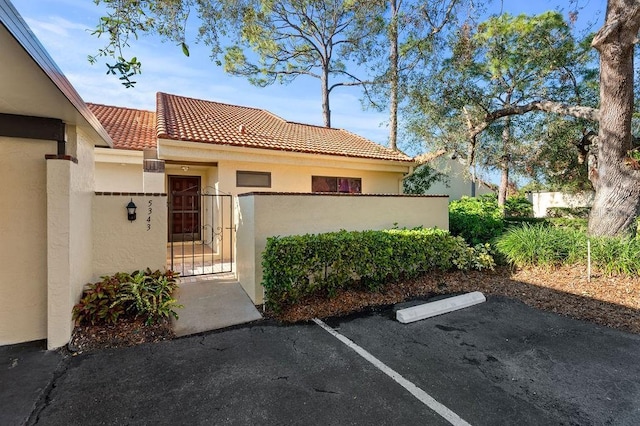 view of front of house featuring a tile roof, fence, a gate, stucco siding, and uncovered parking