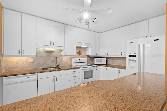 kitchen featuring white appliances, dark stone countertops, under cabinet range hood, and a sink