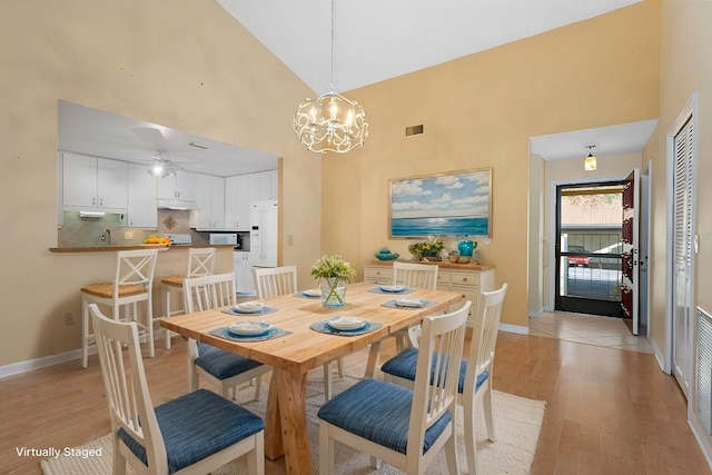 dining room featuring visible vents, a towering ceiling, light wood-style flooring, and baseboards