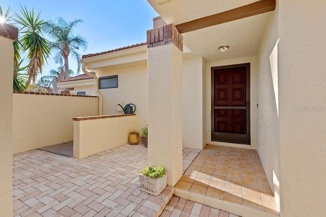 view of exterior entry with a patio, a tile roof, and stucco siding