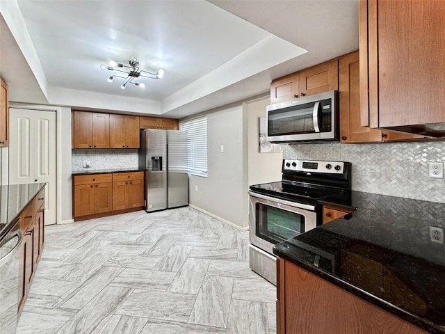 kitchen with decorative backsplash, dark stone counters, stainless steel appliances, and a tray ceiling