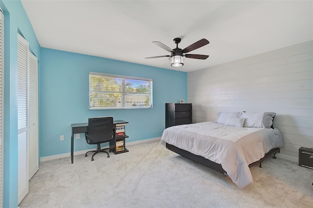 carpeted bedroom with ceiling fan, wood walls, and a closet