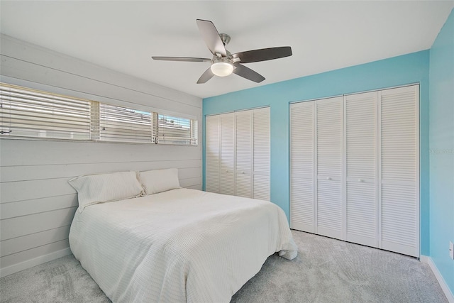 carpeted bedroom featuring ceiling fan, wooden walls, and two closets