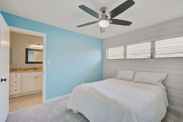 bedroom featuring light carpet, ensuite bathroom, ceiling fan, and wood walls