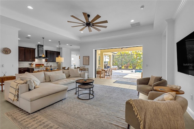 tiled living room featuring ceiling fan, a raised ceiling, and crown molding