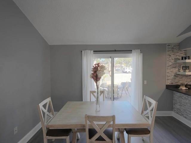 dining space featuring a textured ceiling, dark hardwood / wood-style floors, and vaulted ceiling