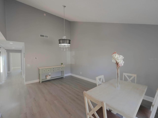 dining space featuring high vaulted ceiling, a notable chandelier, and hardwood / wood-style flooring