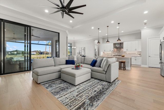 living room with ceiling fan with notable chandelier, light hardwood / wood-style floors, ornamental molding, and sink