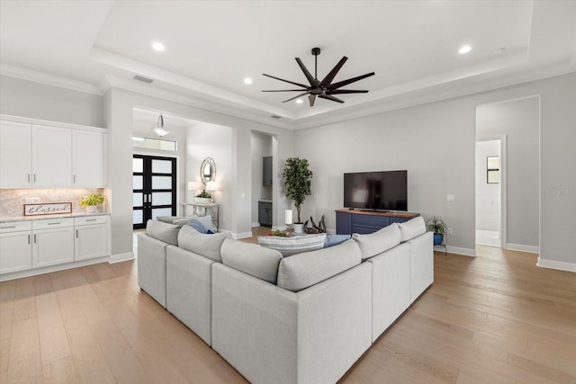 living room featuring ceiling fan, french doors, a raised ceiling, crown molding, and light wood-type flooring