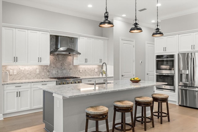 kitchen featuring appliances with stainless steel finishes, a kitchen island with sink, wall chimney exhaust hood, and sink