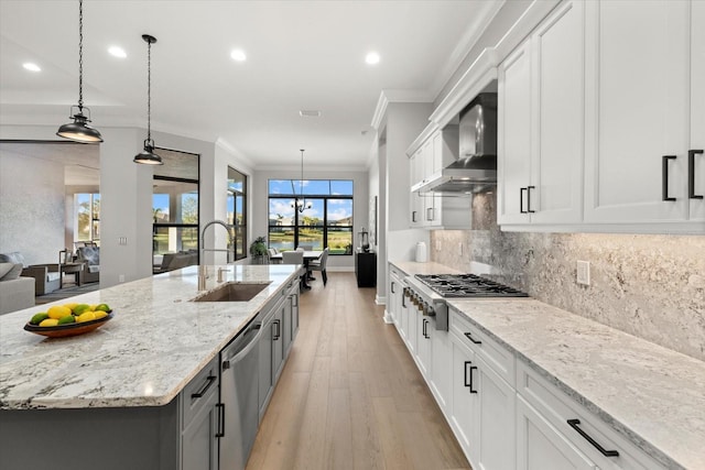 kitchen with white cabinetry, sink, hanging light fixtures, wall chimney range hood, and an island with sink