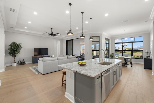 kitchen featuring dishwasher, a kitchen island with sink, ceiling fan with notable chandelier, hanging light fixtures, and light stone countertops