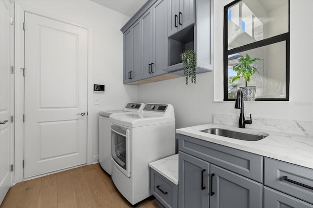 laundry room with cabinets, light wood-type flooring, sink, and washing machine and clothes dryer