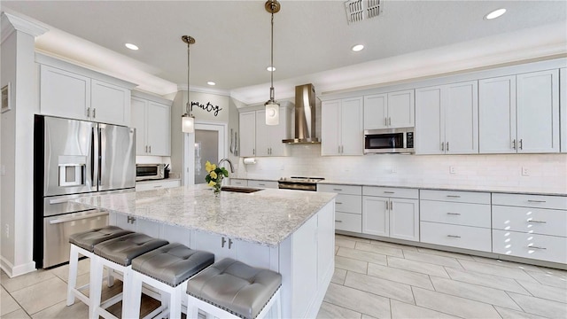 kitchen with sink, wall chimney exhaust hood, hanging light fixtures, stainless steel appliances, and an island with sink