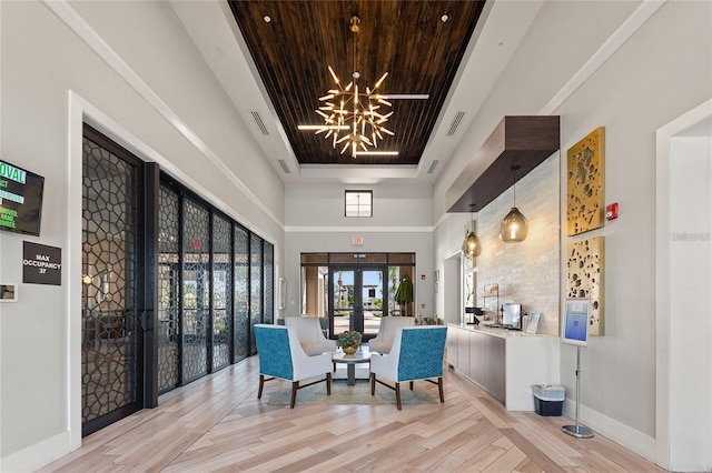 sitting room featuring french doors, a towering ceiling, a raised ceiling, a notable chandelier, and light hardwood / wood-style floors