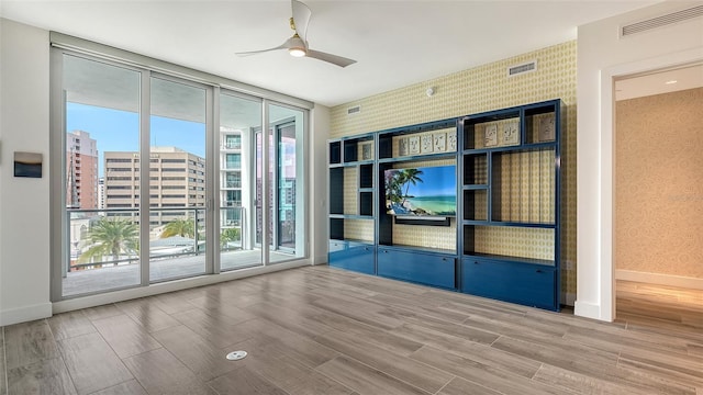 unfurnished room featuring wallpapered walls, baseboards, visible vents, expansive windows, and a view of city