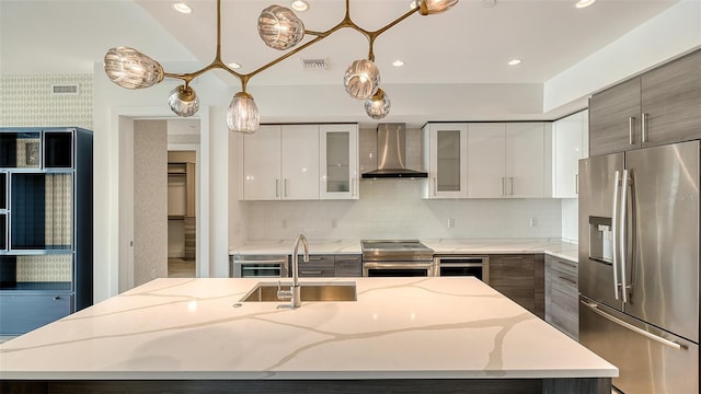 kitchen featuring glass insert cabinets, decorative light fixtures, appliances with stainless steel finishes, wall chimney exhaust hood, and a center island with sink