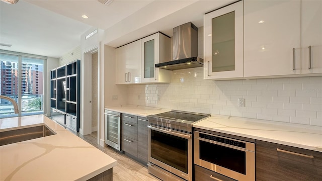 kitchen featuring electric range, beverage cooler, wall chimney range hood, and glass insert cabinets