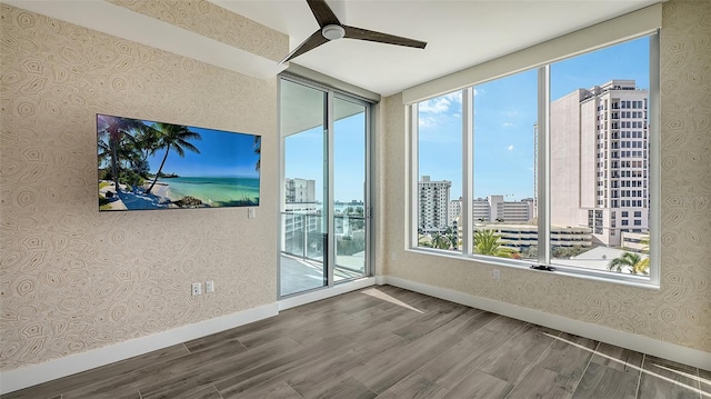 spare room featuring baseboards, wood finished floors, a ceiling fan, and wallpapered walls