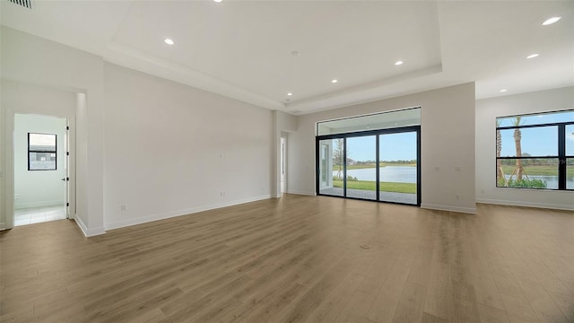 empty room with a raised ceiling, light hardwood / wood-style floors, and a water view