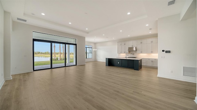 unfurnished living room featuring a notable chandelier, light wood-type flooring, sink, and a tray ceiling