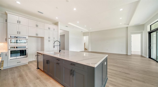 kitchen with white cabinets, stainless steel appliances, an island with sink, light stone counters, and sink