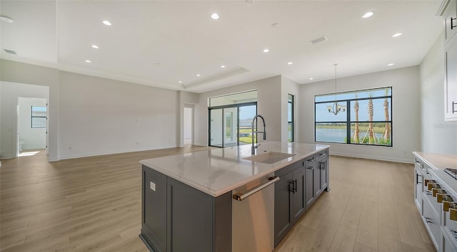 kitchen with an island with sink, light wood-type flooring, sink, an inviting chandelier, and stainless steel dishwasher