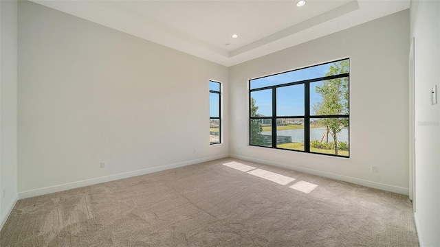 carpeted empty room with a raised ceiling and a water view