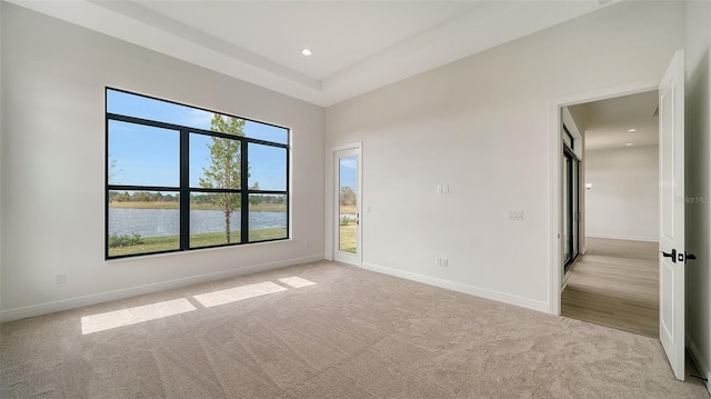 unfurnished room featuring a water view and light carpet