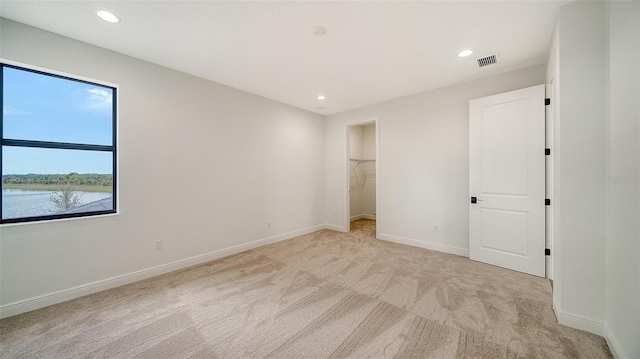 unfurnished bedroom with a walk in closet, a water view, a closet, and light colored carpet