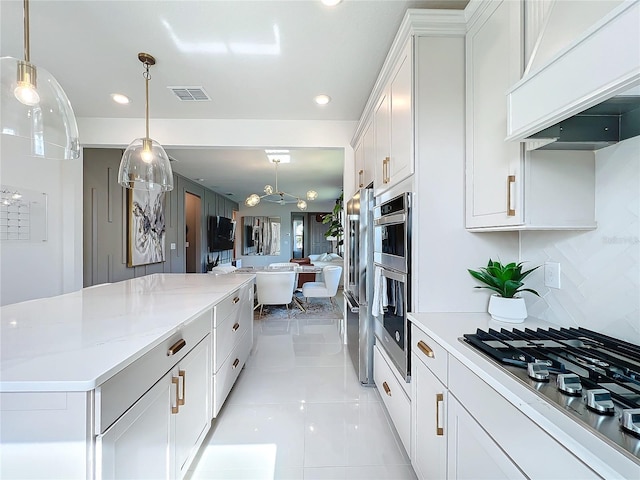 kitchen featuring custom exhaust hood, white gas stovetop, white cabinets, hanging light fixtures, and decorative backsplash