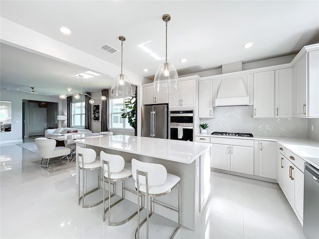 kitchen featuring a kitchen island, backsplash, white cabinets, custom range hood, and appliances with stainless steel finishes