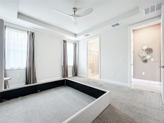 unfurnished bedroom with a raised ceiling, multiple windows, ceiling fan, and carpet floors