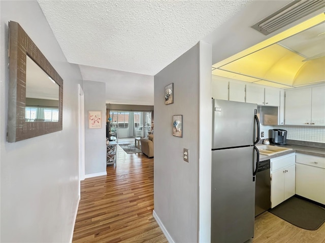 kitchen featuring backsplash, white cabinets, a textured ceiling, appliances with stainless steel finishes, and light hardwood / wood-style floors