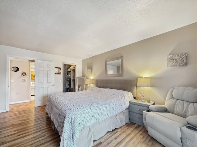 bedroom featuring a textured ceiling, a walk in closet, light hardwood / wood-style flooring, and a closet