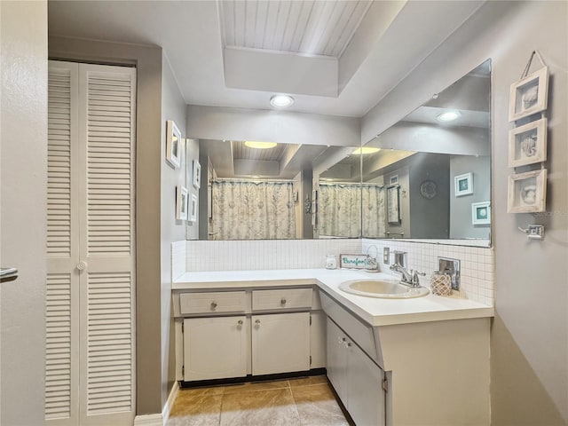 bathroom featuring tile patterned flooring, decorative backsplash, a raised ceiling, and vanity