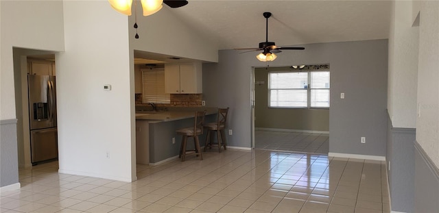 kitchen with light tile patterned flooring, vaulted ceiling, stainless steel fridge, a kitchen breakfast bar, and white cabinets