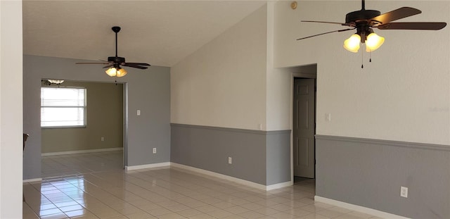 empty room with ceiling fan, vaulted ceiling, and light tile patterned floors