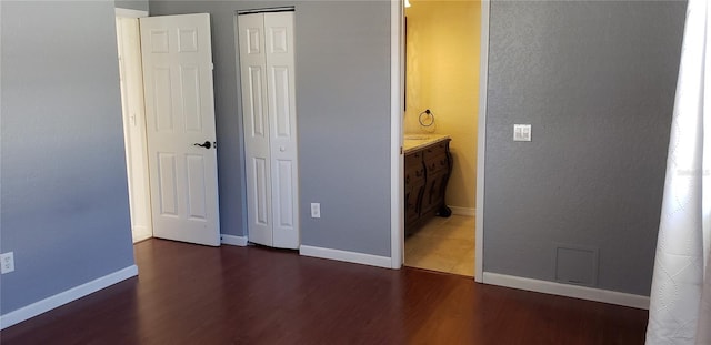 unfurnished bedroom with dark wood-type flooring, ensuite bath, and a closet