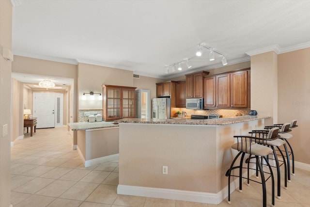 kitchen featuring a breakfast bar, kitchen peninsula, stainless steel appliances, ornamental molding, and light stone counters