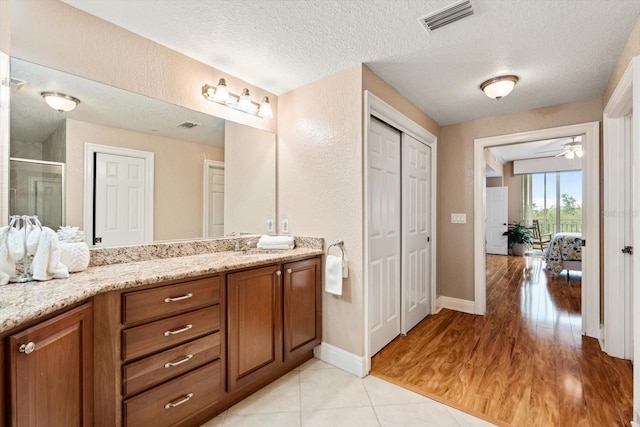 bathroom featuring a shower with shower door, hardwood / wood-style flooring, ceiling fan, a textured ceiling, and vanity